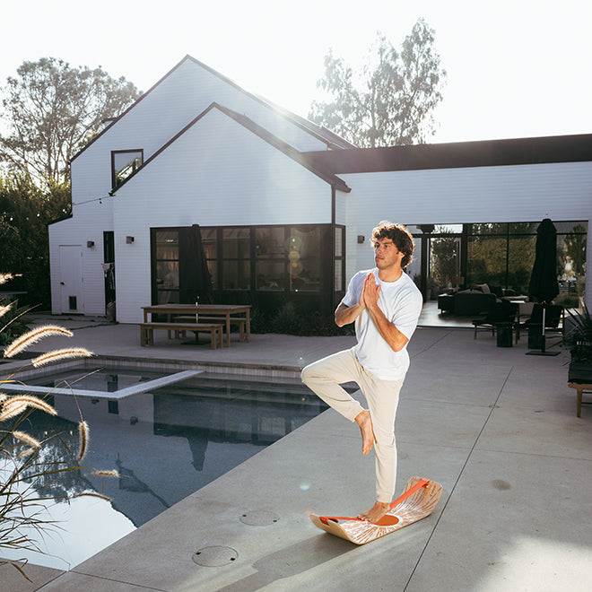 Person practicing yoga on a sunbeam slackboard poolside with a modern house in the background