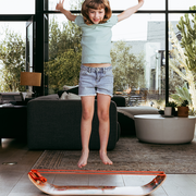 Child jumping off of a unicorn slackboard plus in a living room