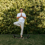 Person practicing yoga in a tree pose using a caesar slackboard plus. against a green bush background.