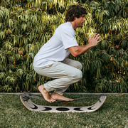 Man balancing on a Moon SlackBoard Plus outdoors with greenery in the background