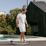 Man standing on a mountain slackboard plus by a pool with a modern house and trees in the background
